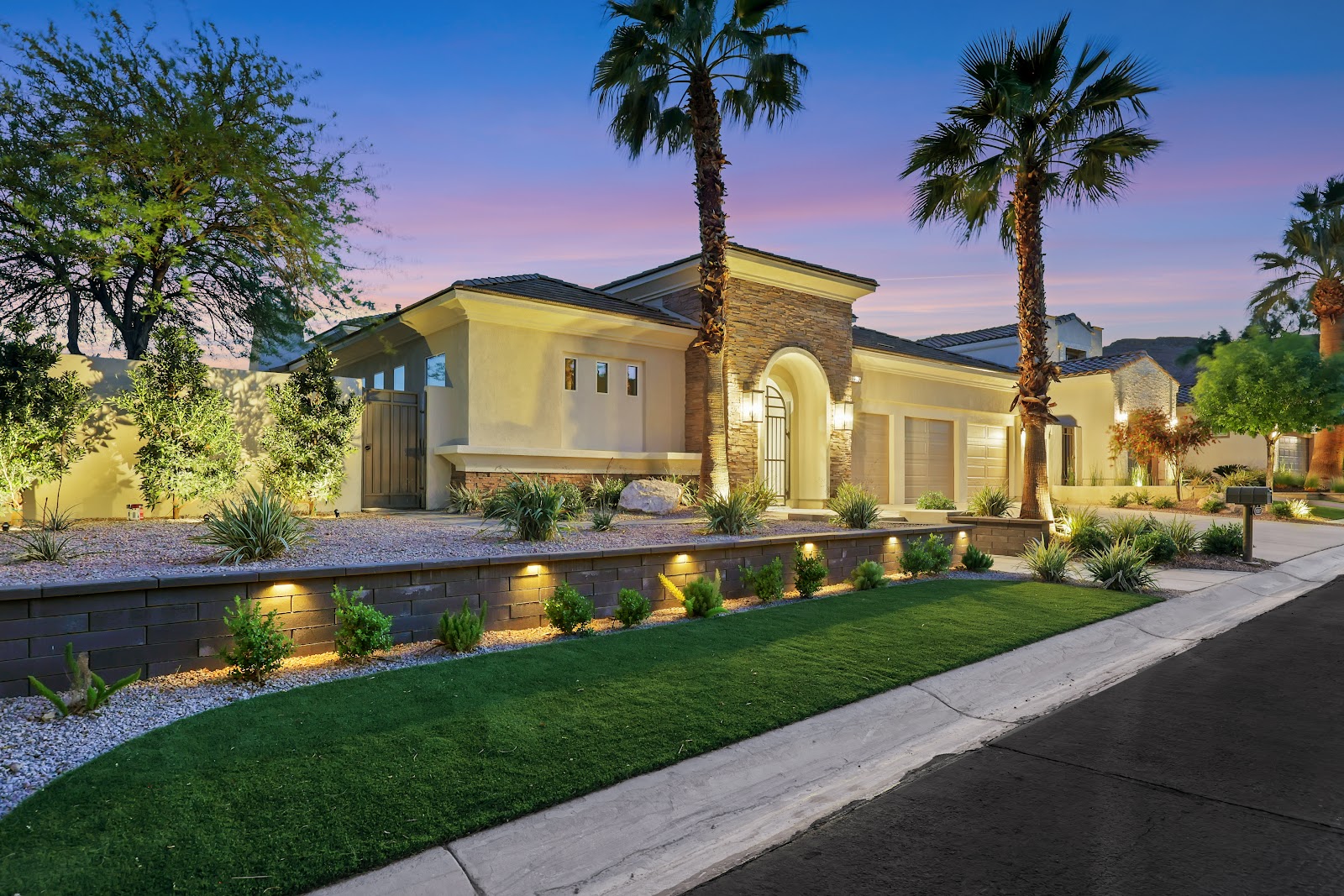 Luxury home at dusk with landscape lighting, a turf lawn and a retaining wall