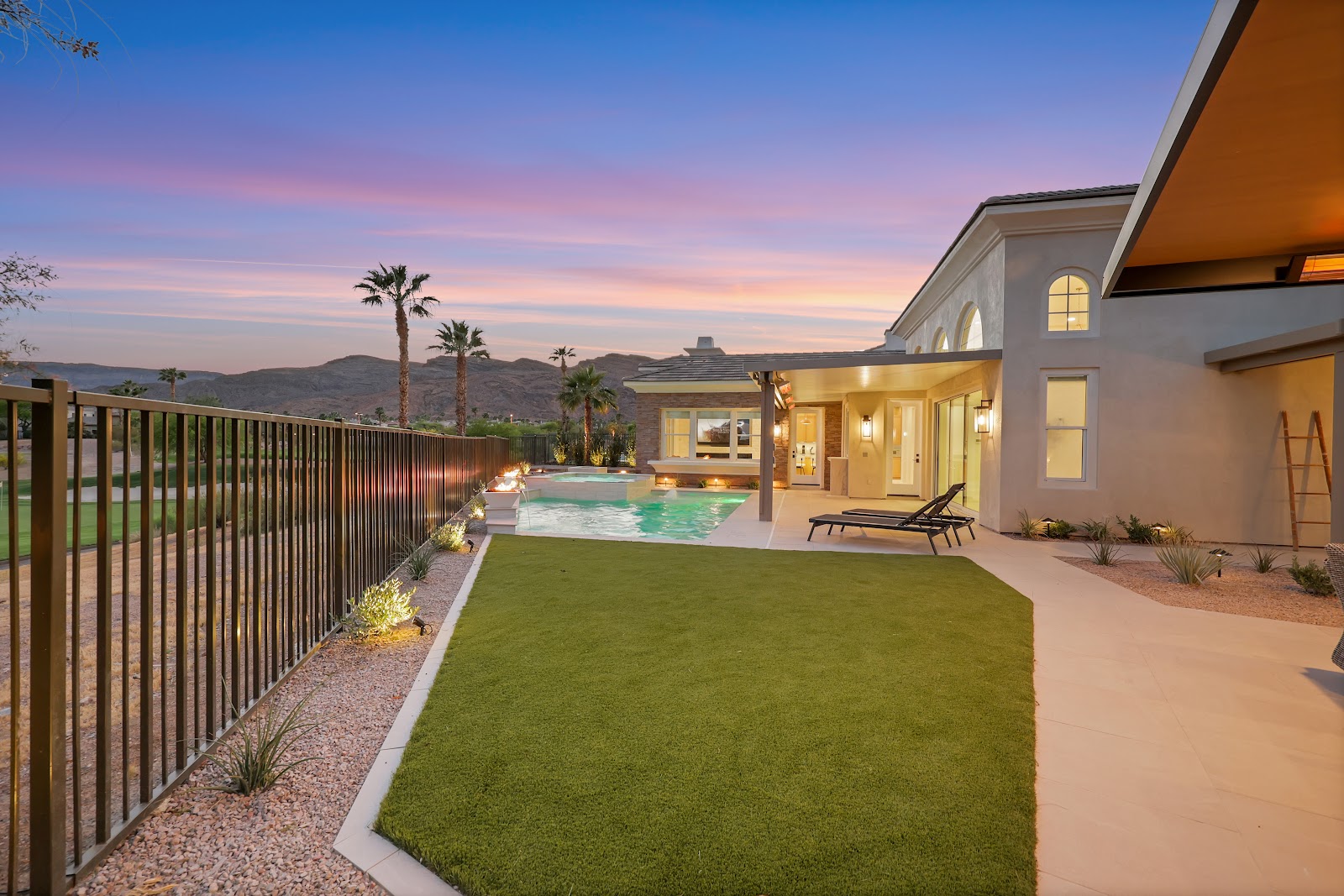 Backyard with a turf lawn, pool and patio at sunset with golf course and mountain views