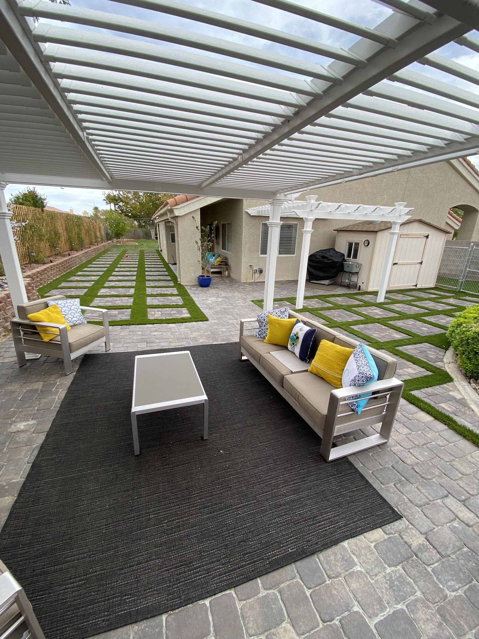 Covered patio with a pergola, paver flooring and a turf-and-paver checkerboard yard
