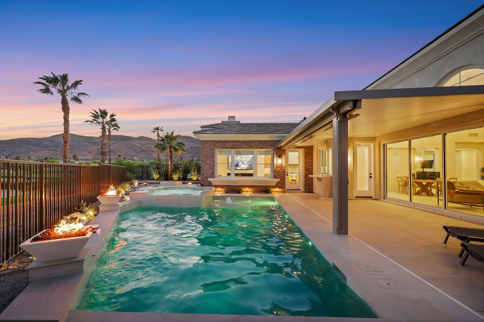 Backyard pool with fire bowls and a covered patio at sunset with a mountain view